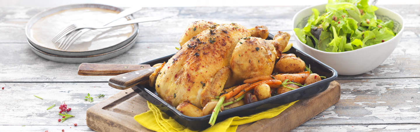 Poulet rôti et ses légumes rôtis disposé sur une planche en bois et accompagné d’un bol de salade