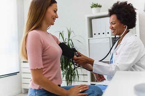 Médecin prend la tension d’une femme, toutes deux souriantes