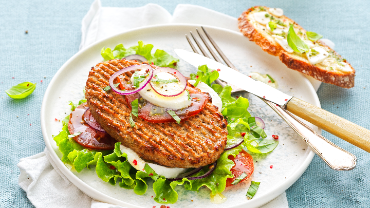 Visuel recette d'un burger de soja estival sur un lit de salade, tomates et burrata