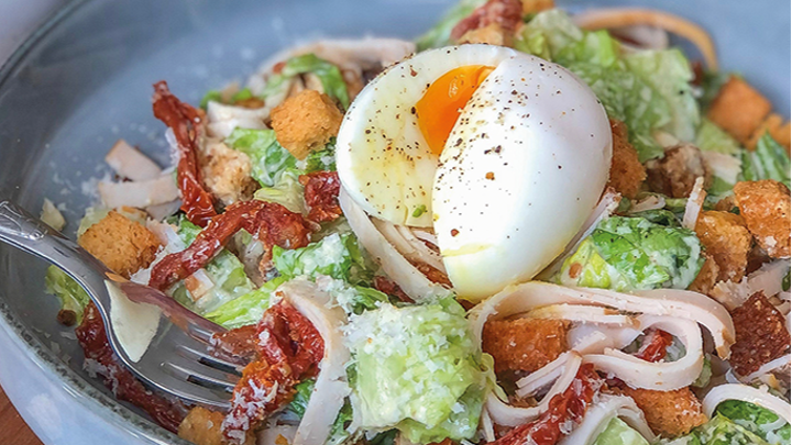 Visuel recette d'une salade César au blanc de poulet, agrémentée de tomates séchées, d'œuf dur, de croûtons de pain et de parmesan