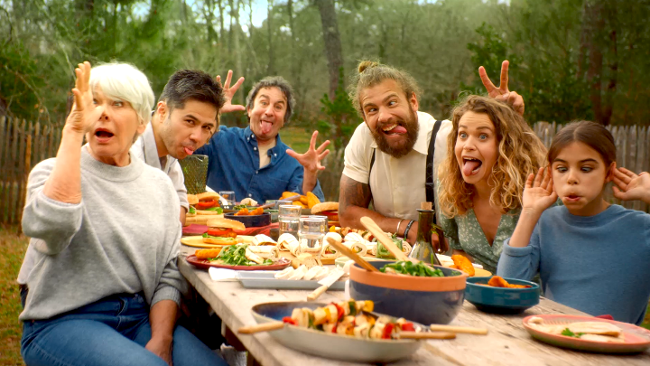 Repas de famille convivial en extérieur, avec des plats gourmands à base de volaille sur une table de pique-nique tout en faisant des grimaces